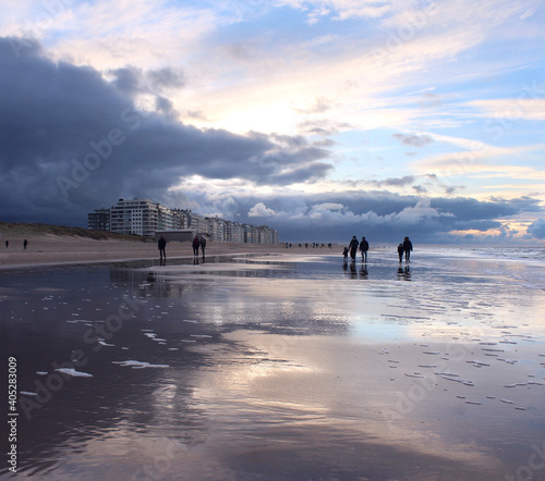 Silhouetted people walking on the sandy beach during a winters sunset at Wenduine, West Flanders, Belgium