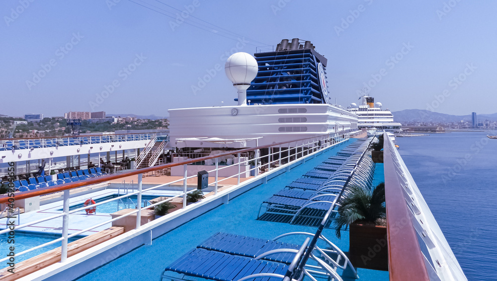 Obraz premium Vue du pont supérieur et des transats d'un navire de croisière en escale au terminal du port de Marseille.