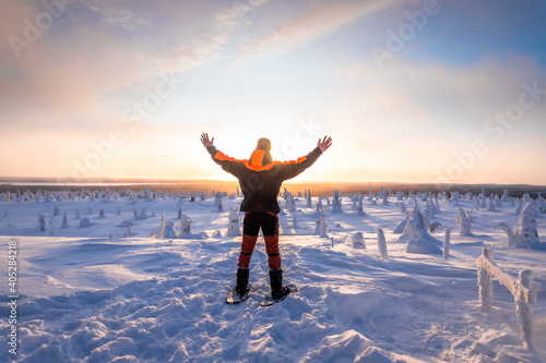 Man in snowshoes in front of a Snowy landscape with his arms open. In a sunset.