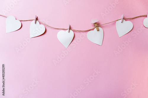 White paper hearts hang on a clothesline with clothespins on a pink background, copying the space. Beautiful, festive background