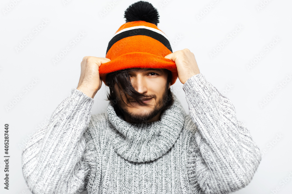 Studio portrait of young guy holding hands on orange hat, on white background.