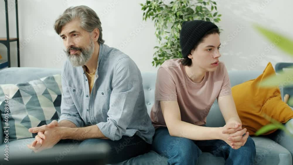 Portrait of unhappy family father and son sitting on couch back to back in silence sighing feeling sad and uncomfortable. Relations and emotions concept. Portrait of unhappy family father and son sitting on couch back to back in silence sighing feeling sad and uncomfortable. Relations and emotions concept.