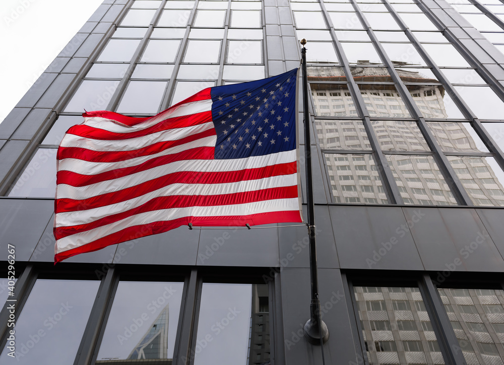 Large USA flag waving in front of a tall city building.