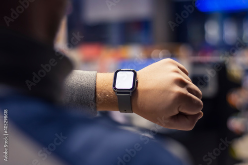 A man with a smartwatch and a white screen mockup on his hand. A man uses a fitness tracker on the background of a shopping mall.