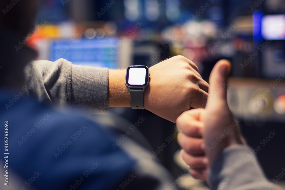A man with a smartwatch and a white screen mockup on his hand. A man uses a fitness tracker on the background of a shopping mall. A man with a smartwatch and a white screen mockup on his hand. A man uses a fitness tracker on the background of a shopping mall.