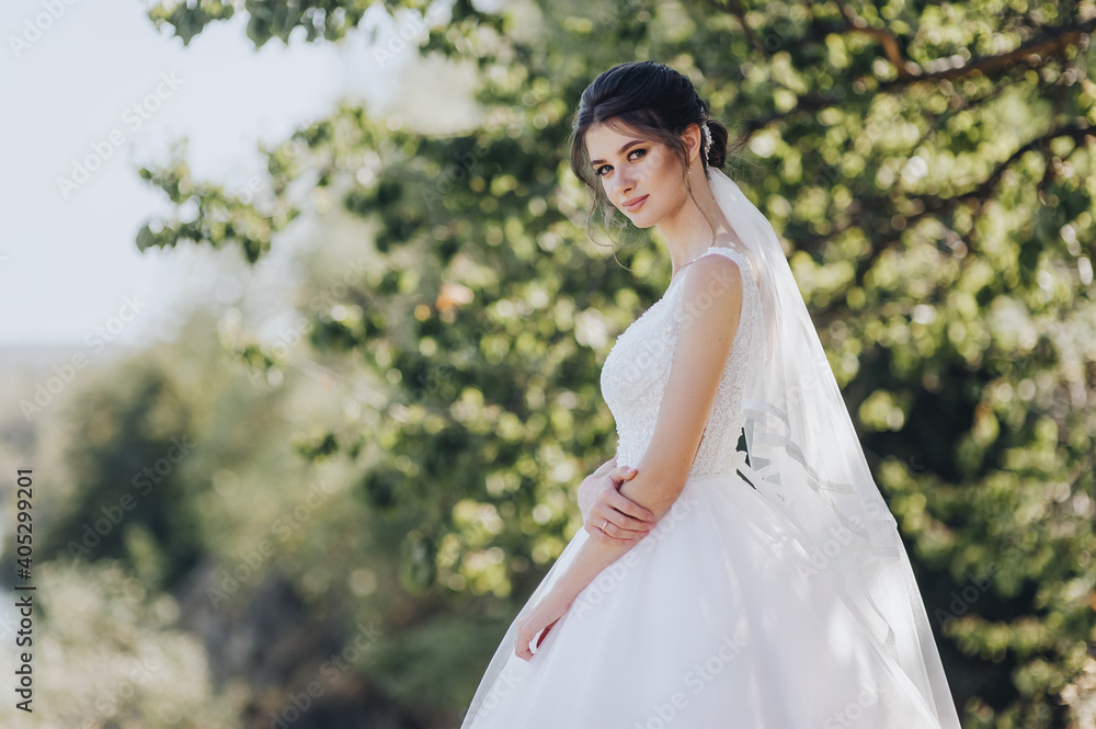 Wedding portrait of a beautiful brunette bride with curly hair in a white dress in nature, against the background of a tree in greenery. Wedding portrait of a beautiful brunette bride with curly hair in a white dress in nature, against the background of a tree in greenery.