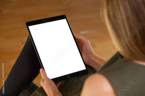 Attentive young woman holding tablet with white screen in vertical orientation. Concept of communicating through modern wireless digital device. Rear close-up view of person using electronical device.