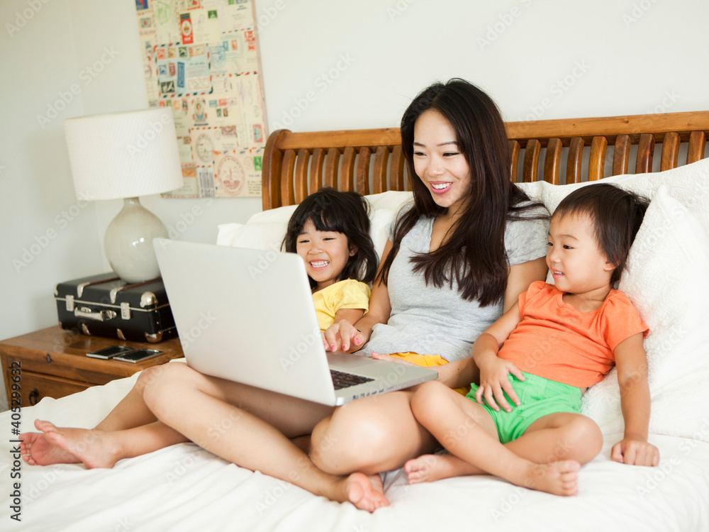 Mother with daughters (2-3, 4-5) sitting on bed, using laptop Mother with daughters (2-3, 4-5) sitting on bed, using laptop