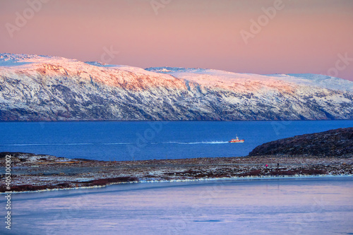 Amazing sunrise polar landscape with white snowy mountain range on the horizon. Wonderful mountain landscape on the Barents sea.