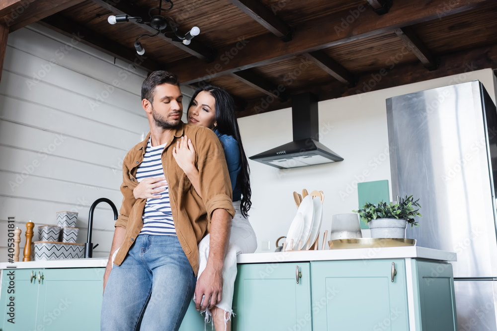happy young woman sitting on kitchen counter and embracing boyfriend happy young woman sitting on kitchen counter and embracing boyfriend
