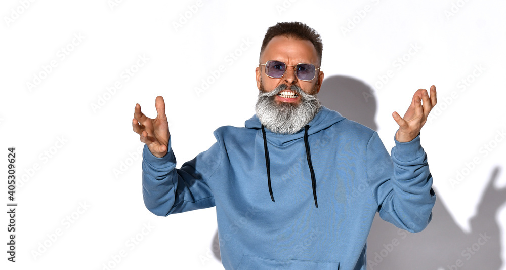 Naklejka premium Irritated emotional gray-haired bearded man in fashionable sunglasses, casual sweatshirt looks into the camera with irritation. People, negative emotions and feelings. Studio shot isolated on white