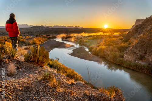 A man, person, visitor standing on a cliff watching the sunrise over distance mountains and a river meandering below, Rio Grande River, Big Bend National Park, Texas