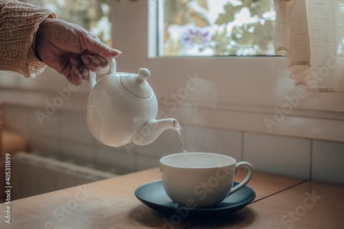 Woman's hand serving tea in cup on kitchen table photo