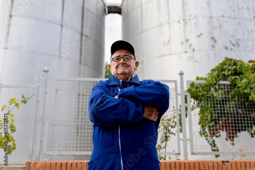 Elderly male winemaker with arms crossed against stainless steel vat at winery industry photo