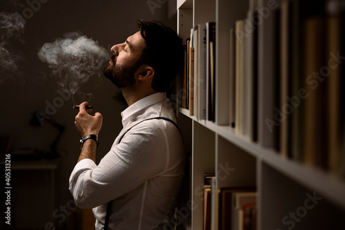 Portrait of bearded man smoking cigar in front of bookshelf photo