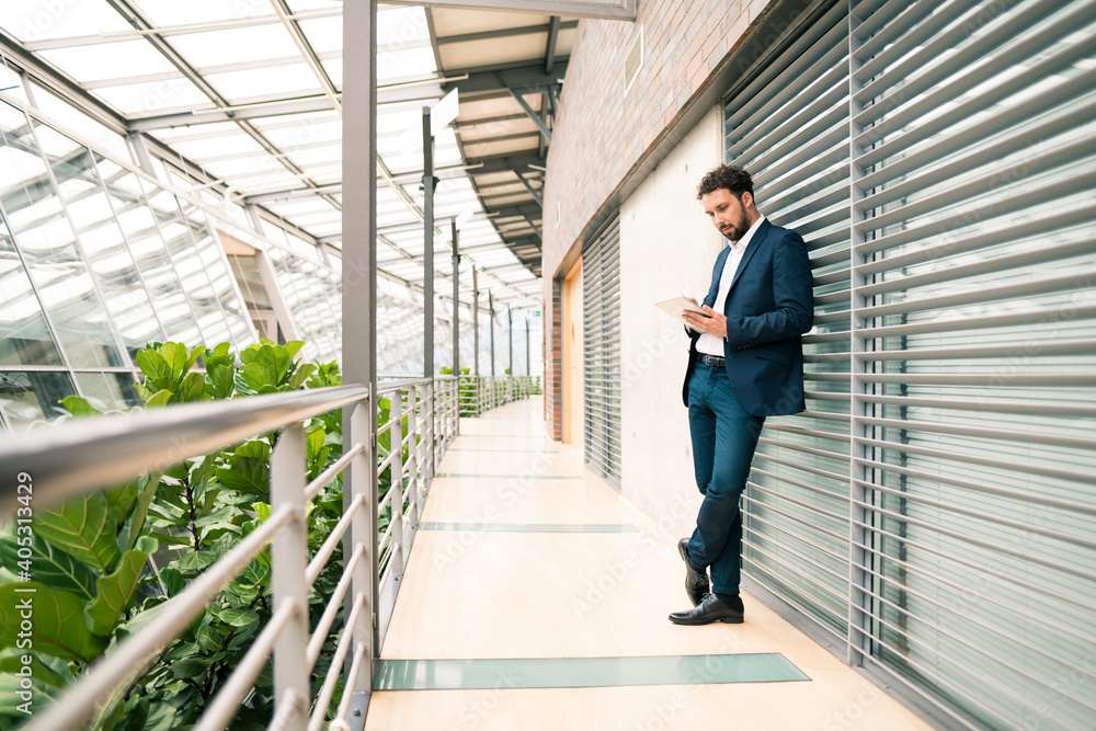Businessman using digital tablet while leaning against wall in corridor at office Businessman using digital tablet while leaning against wall in corridor at office