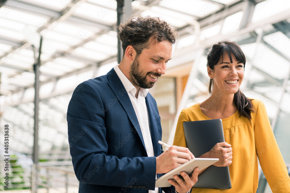 Smiling male colleague using digital tablet standing by female entrepreneur at office Smiling male colleague using digital tablet standing by female entrepreneur at office