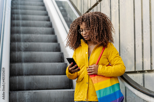 Woman with multi colored purse using mobile phone while standing on escalator in city photo