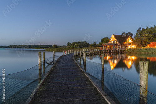 Germany, Schleswig-Holstein, Hemmelsdorf, Empty pier on shore of¬†Hemmelsdorfer¬†See lake at dawn with house in background photo