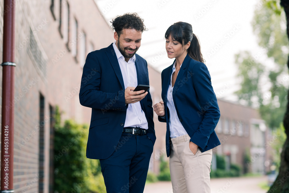 Businessman using smart phone standing by female colleague standing in office park Businessman using smart phone standing by female colleague standing in office park
