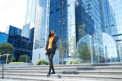 Female professional walking on steps while talking on phone against office building photo