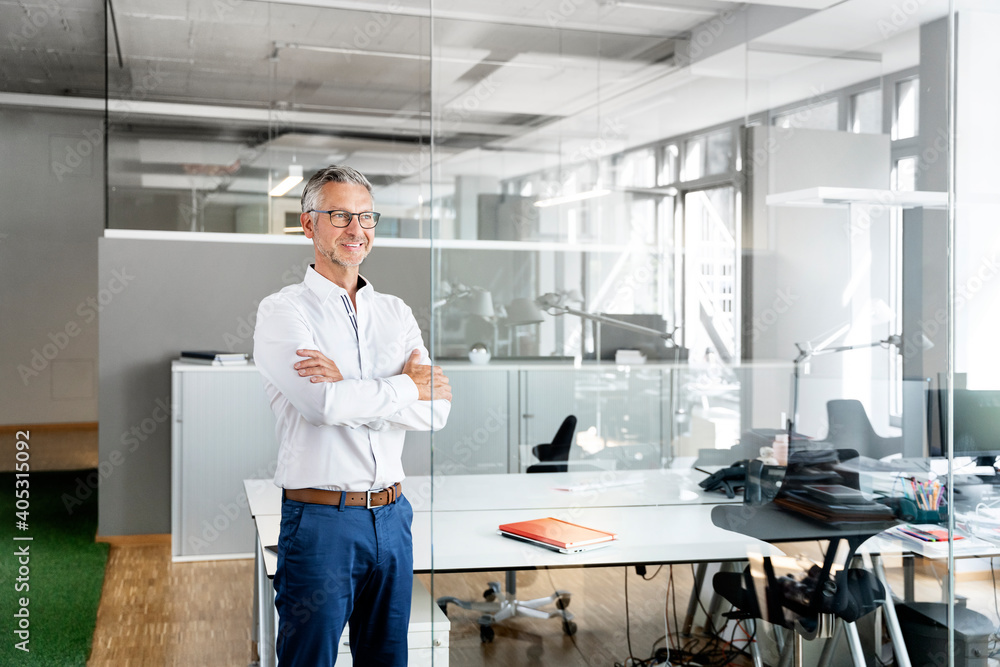 Smiling businessman with arms crossed day dreaming in office Smiling businessman with arms crossed day dreaming in office
