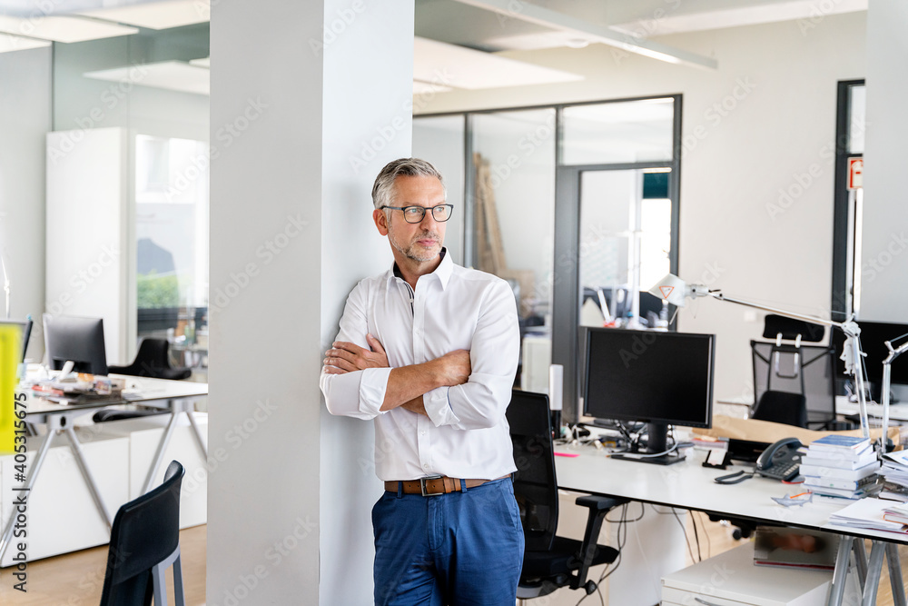 Confident businessman with arms crossed leaning on column in office Confident businessman with arms crossed leaning on column in office