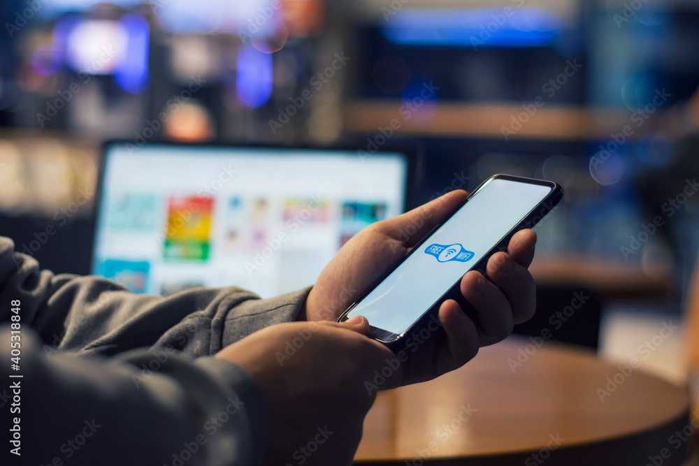 Man freelancer holds a smartphone with free internet in his hands on the background of a laptop. Man freelancer holds a smartphone with free internet in his hands on the background of a laptop.