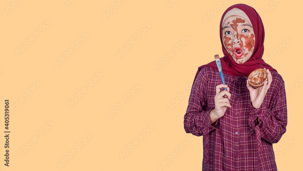 Asian woman with hijab on head and facial mask looking at the copyspace over orange background. Woman spa mask beauty concept. copyspace for text