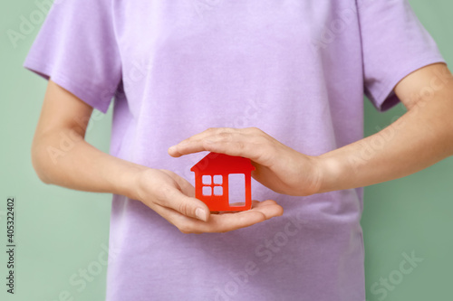 Female hands with figure of house on color background