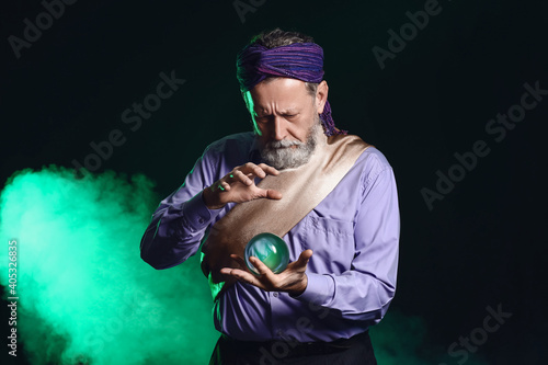 Male fortune teller with crystal ball on dark background photo