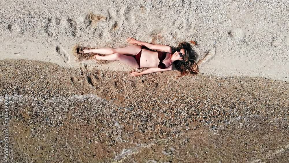 Young woman sitting on the beach sand near water and relaxing. Top view Young woman sitting on the beach sand near water and relaxing. Top view