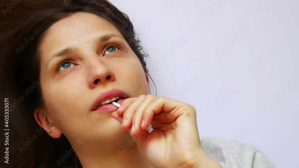 Close-up of the face of a beautiful girl lying on a white surface and sucking a lollipop while thinking about something Close-up of the face of a beautiful girl lying on a white surface and sucking a lollipop while thinking about something