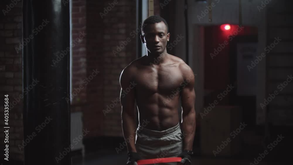 A black handsome man pumping his hands muscles in the gym - pulling the belt attached to weights A black handsome man pumping his hands muscles in the gym - pulling the belt attached to weights