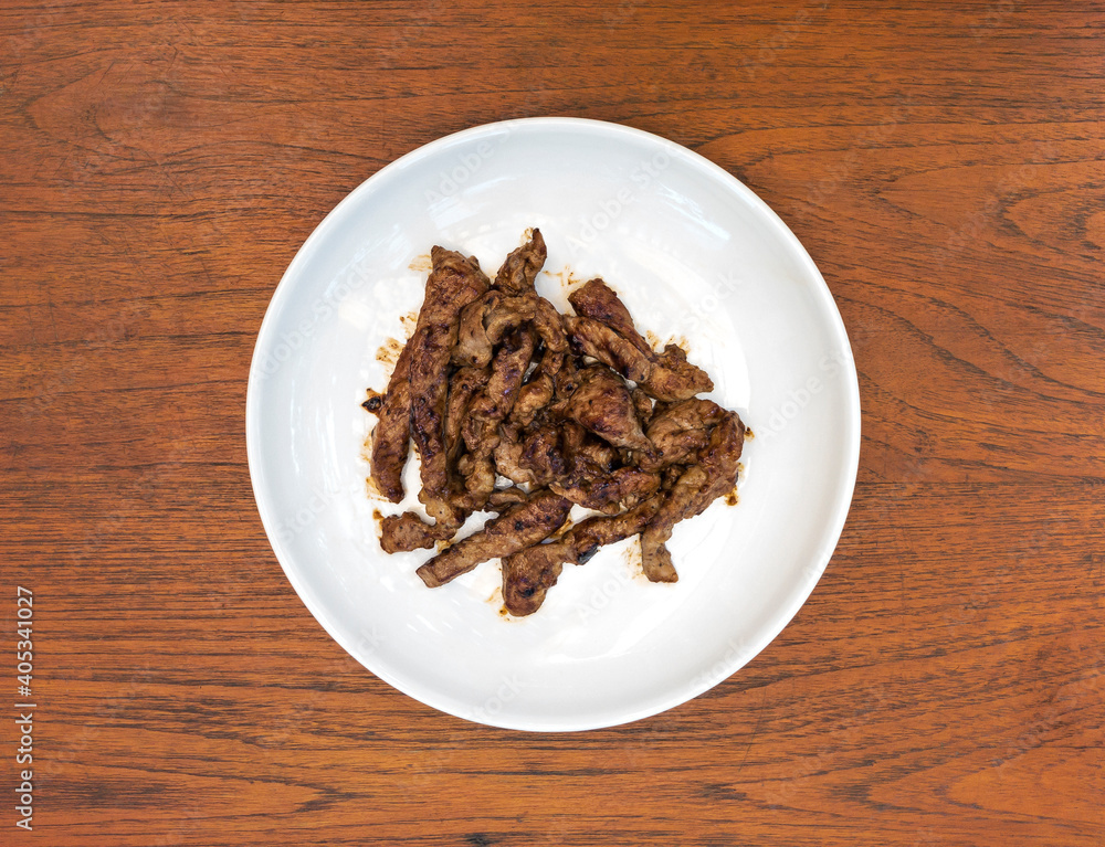 Fried marinated pork on white round ceramic plate. On the wooden background. Fried marinated pork on white round ceramic plate. On the wooden background.