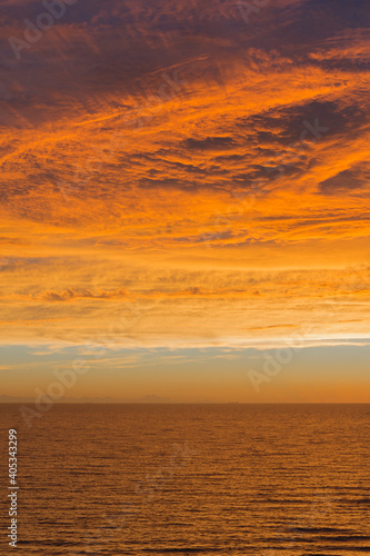 Vista de paisaje de mar y cielo con nubes iluminadas de colores naranja y dorado del atardecer y amanecer 