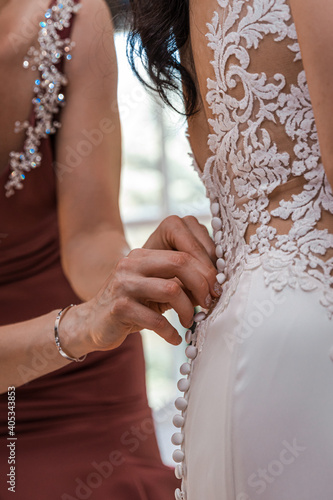 Bridesmaids buttoning up bride's dress