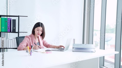 Focused concentrated Asian businesswoman professional worker writing notes research planning thinking ideas strategy, employee working in modern office using laptop computer, side view copyspace