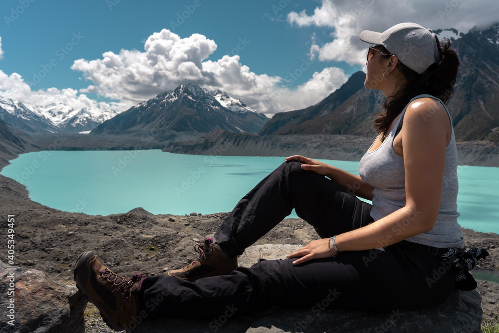 Brunette woman resting on a rock and looking at Tasman lake and mount. New Zealand