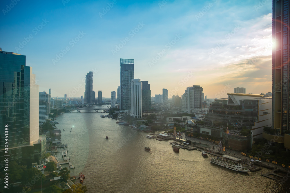 The Chao Phraya River flows through Bangkok in the Sathorn area, with bridges over the river and boats when the sun is setting.