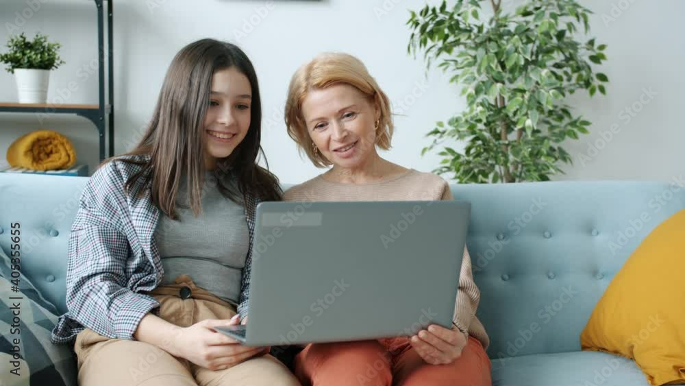Happy teenage daughter and mother are making video call from apartment waving hand smiling enjoying internet communication with laptop computer Happy teenage daughter and mother are making video call from apartment waving hand smiling enjoying internet communication with laptop computer