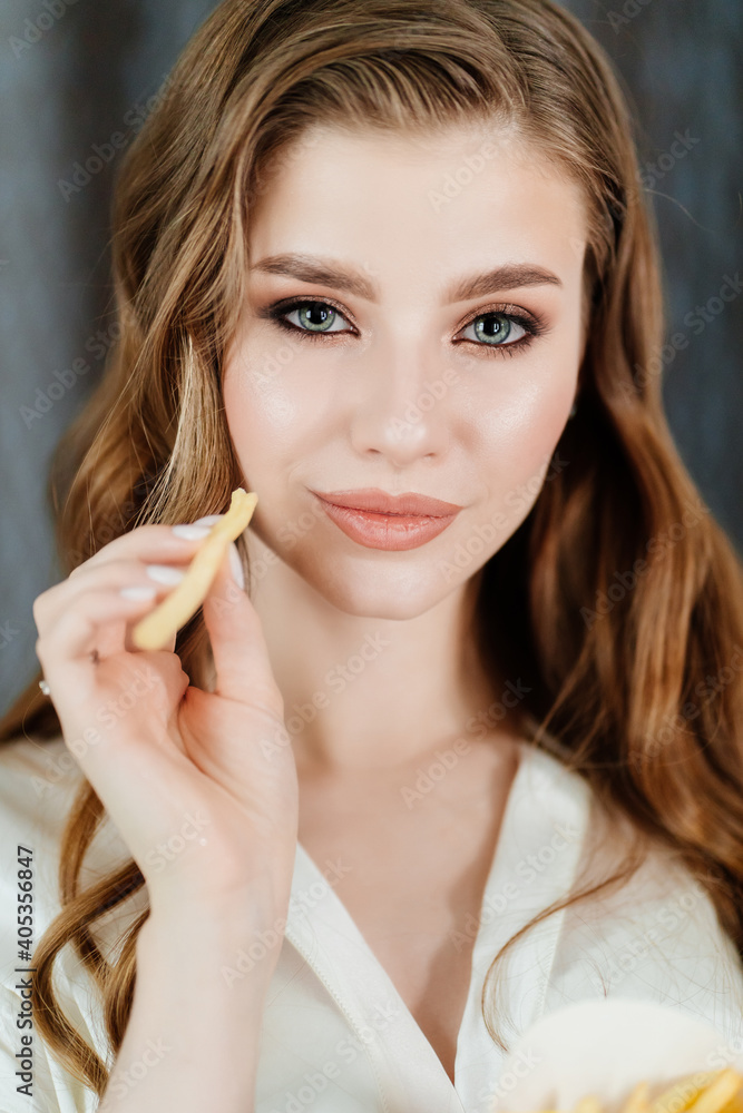 beautiful young woman with long hair and makeup eating French fries. beautiful young woman with long hair and makeup eating French fries.