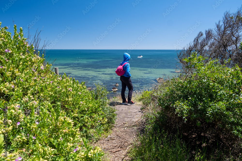 Tourist in blue hoodie standing in front of beautiful shallow ocean bay admiring the view