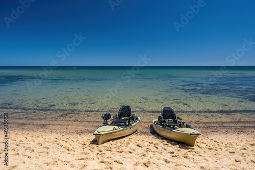 Two fishing kayaks on a beach with beautiful turquoise shallow water and copy space