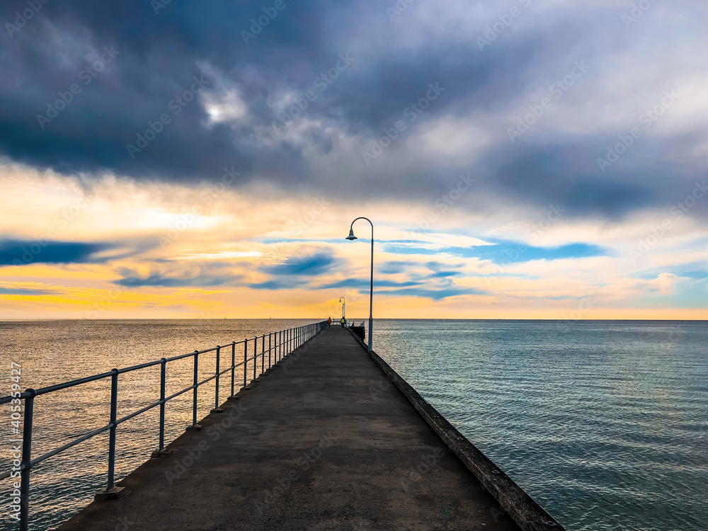 Pier stretching into the ocean with light poles at sunset in diminishing perspective
