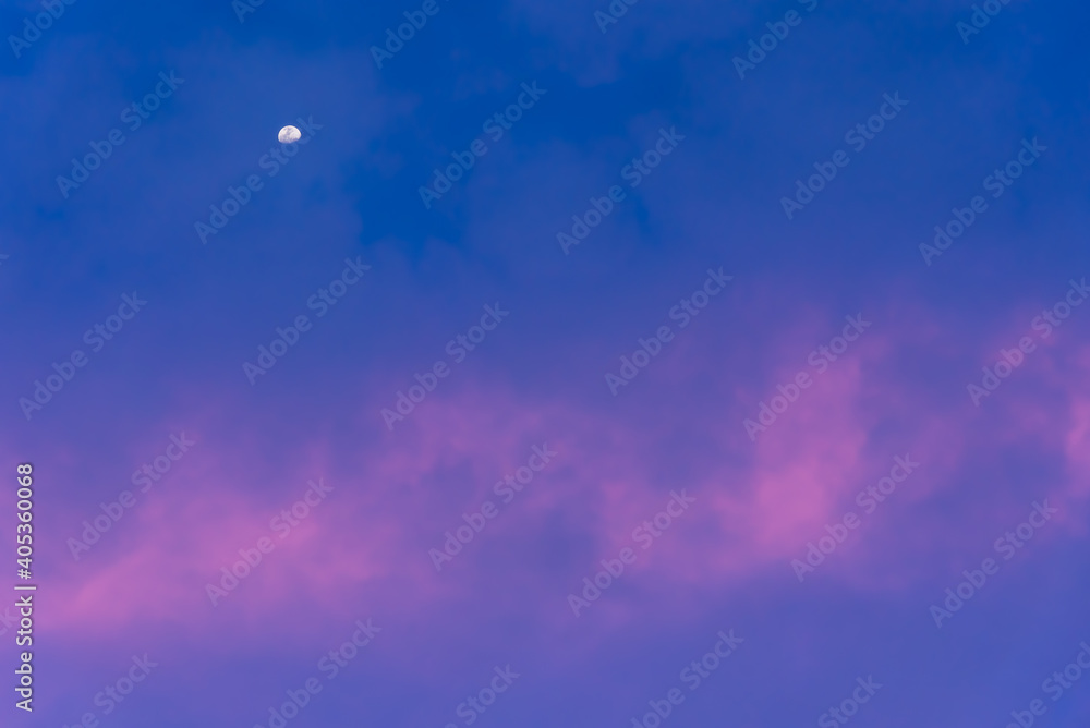 A distant moon in the early evening sky with lite pink clouds capturing the last of the sunlight for the day A distant moon in the early evening sky with lite pink clouds capturing the last of the sunlight for the day