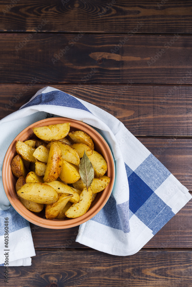Slices of baked potatoes with herbs in a plate on a kitchen towel and a wooden table. Vertical orientation, no people, copy space, close-up Slices of baked potatoes with herbs in a plate on a kitchen towel and a wooden table. Vertical orientation, no people, copy space, close-up