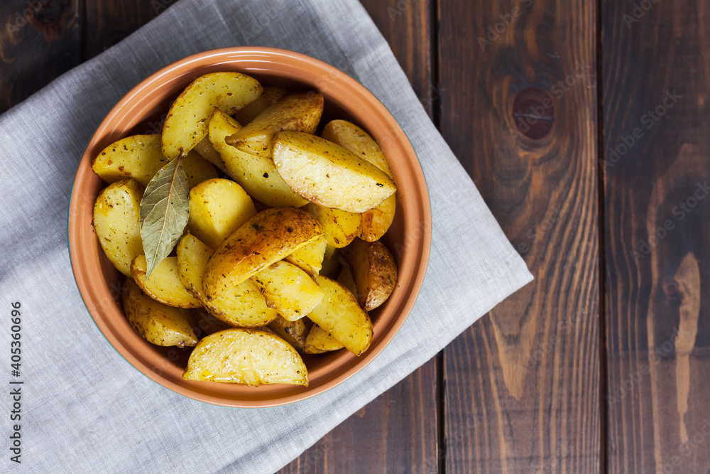 Slices of baked potatoes with herbs in a plate on a kitchen towel and a wooden table. Horizontal orientation, no people, copy space, close-up Slices of baked potatoes with herbs in a plate on a kitchen towel and a wooden table. Horizontal orientation, no people, copy space, close-up