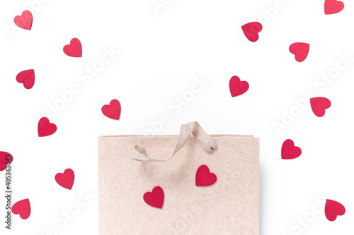 The paper shopping bag is on a white background and decorated with red wooden heart-shaped figures. Valentine's day shopping concept. Flat lay. Top view. Copy space.