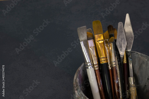 Paint brushes in a bucket. Dark textured background.